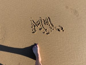 Initials drawn in wet sand on the beach, with a woman's foot 