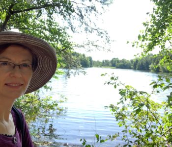 woman in hat by lake with trees