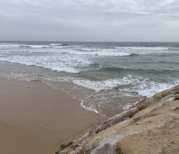 A beach scene with sand, the ocean, rocks and a cloudy sky.