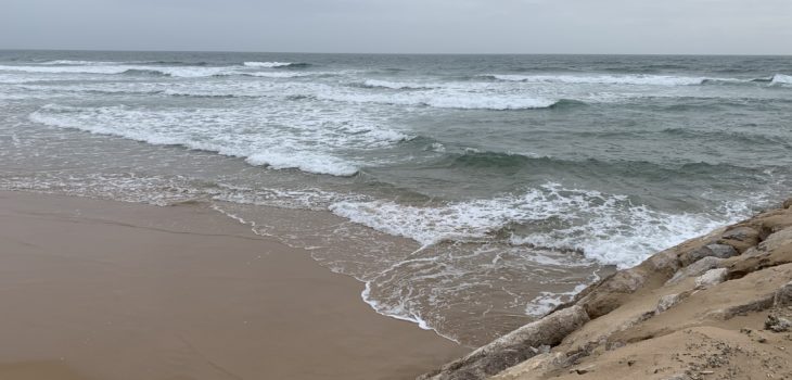 A beach scene with sand, the ocean, rocks and a cloudy sky.