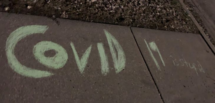 "COVID-19 is stupid" spelled in chalk on a sidewalk.